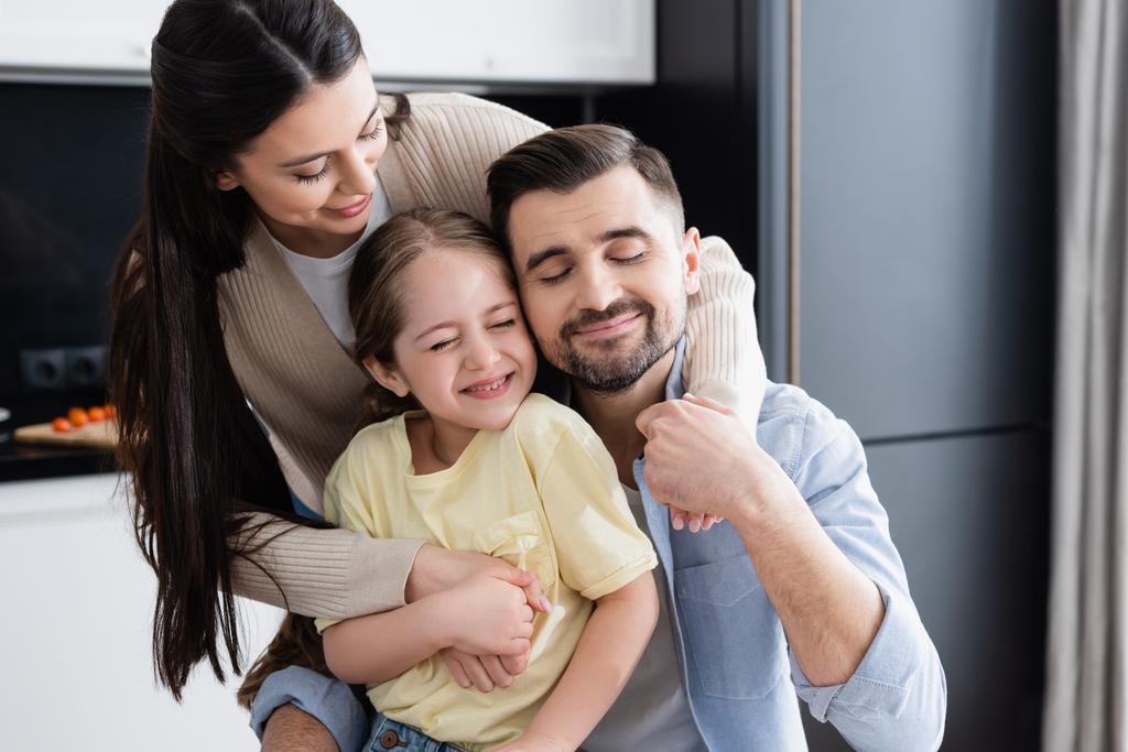 família feliz com olhos fechados abraçando na cozinha - Foto, Imagem