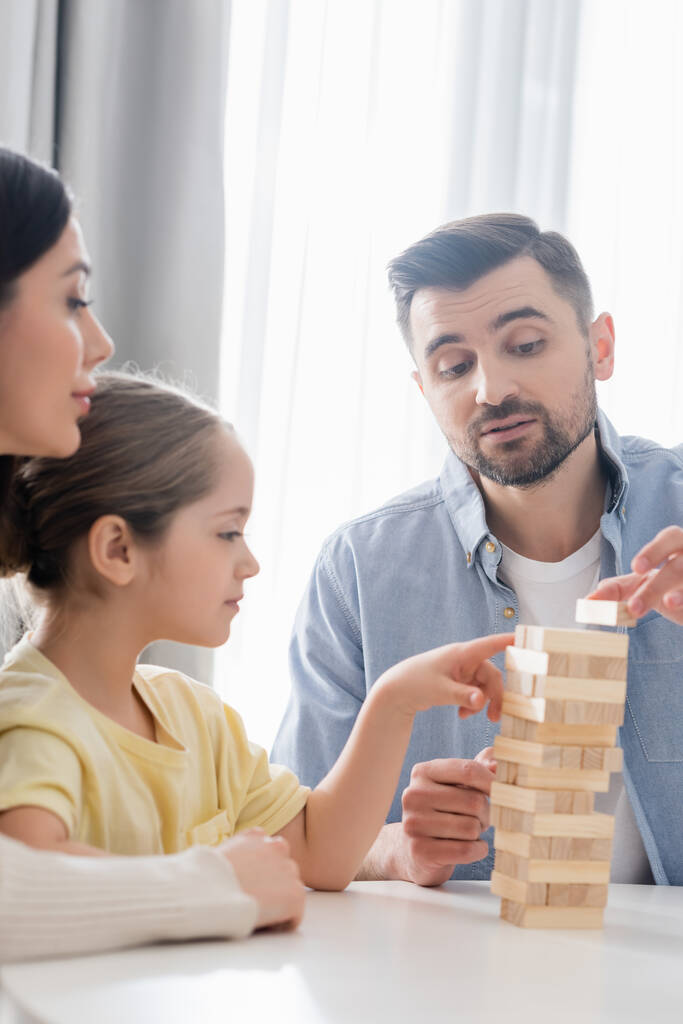 girl pointing with finger at wooden tower while playing together with parents - Photo, Image