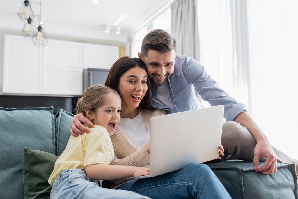 podekscytowana para z córką oglądającą film na laptopie w domu - Zdjęcie, obraz