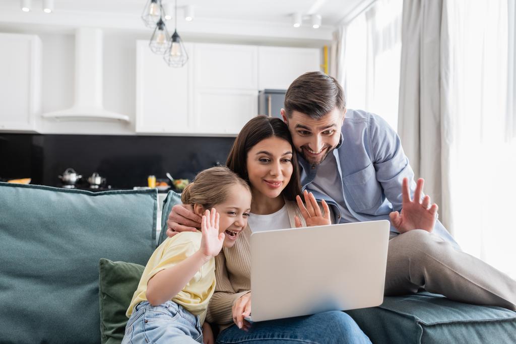 cheerful couple with daughter waving hands during video call on laptop - Photo, Image