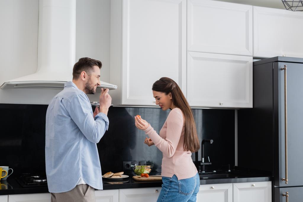 vidám férfi kezében csészealj fedél közel boldog feleség készít reggelit  - Fotó, kép