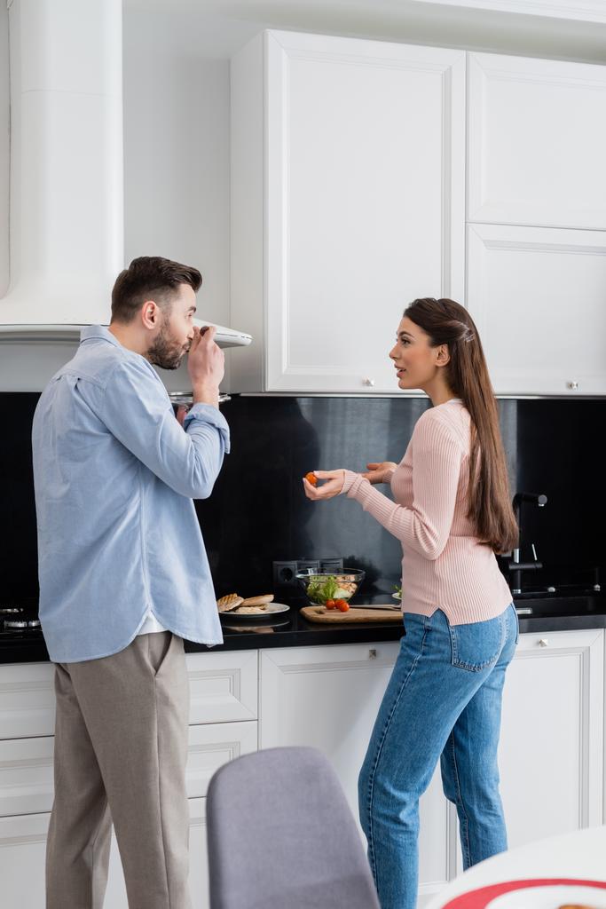 donna che parla con marito degustazione pasto in cucina - Foto, immagini