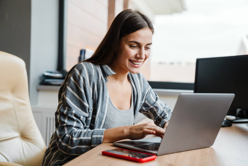 Bájos boldog nő mosolyog, miközben dolgozik laptop otthon - Fotó, kép