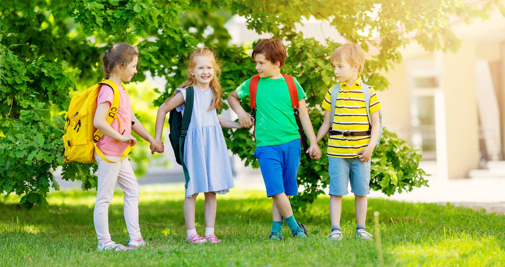 Aranyos gyerekek hátizsákkal a parkban állnak az iskola mellett. - Fotó, kép