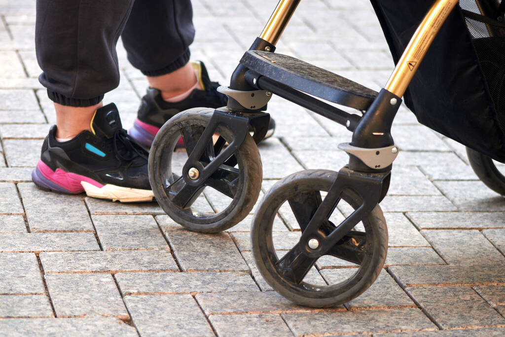wheels of a baby carriage and woman in sneakers standing on the cobblestones.  - Photo, Image