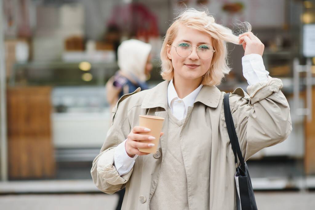 Güzel stil sahibi bir kadın güzel kıyafetlerle sokakta yürüyor ve kahvesini fincanda içiyor. İyi bir yaz havası var, sokak kafesi yakınlarında.. - Fotoğraf, Görsel