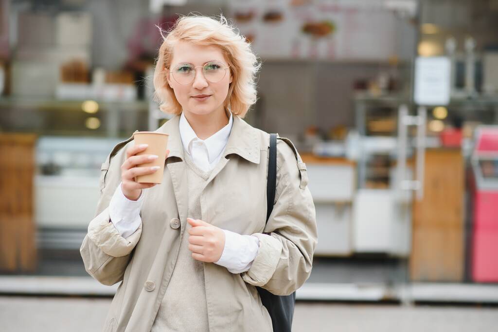 schöne stilvolle Frau mit guter Mode Kleidung zu Fuß auf der Straße und trinken etwas Kaffee in Tasse zum Mitnehmen mit guter Sommerstimmung in der Nähe Straßencafé. - Foto, Bild