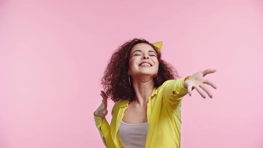 potěšená mladá žena ve straně čepice s nataženou rukou izolované na růžové  - Fotografie, Obrázek