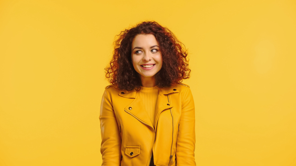 pleased young and curly woman looking away isolated on yellow - Photo, Image
