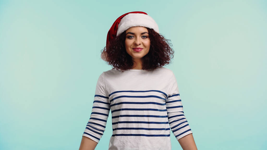 glückliche junge Frau mit Weihnachtsmütze isoliert auf blau  - Foto, Bild