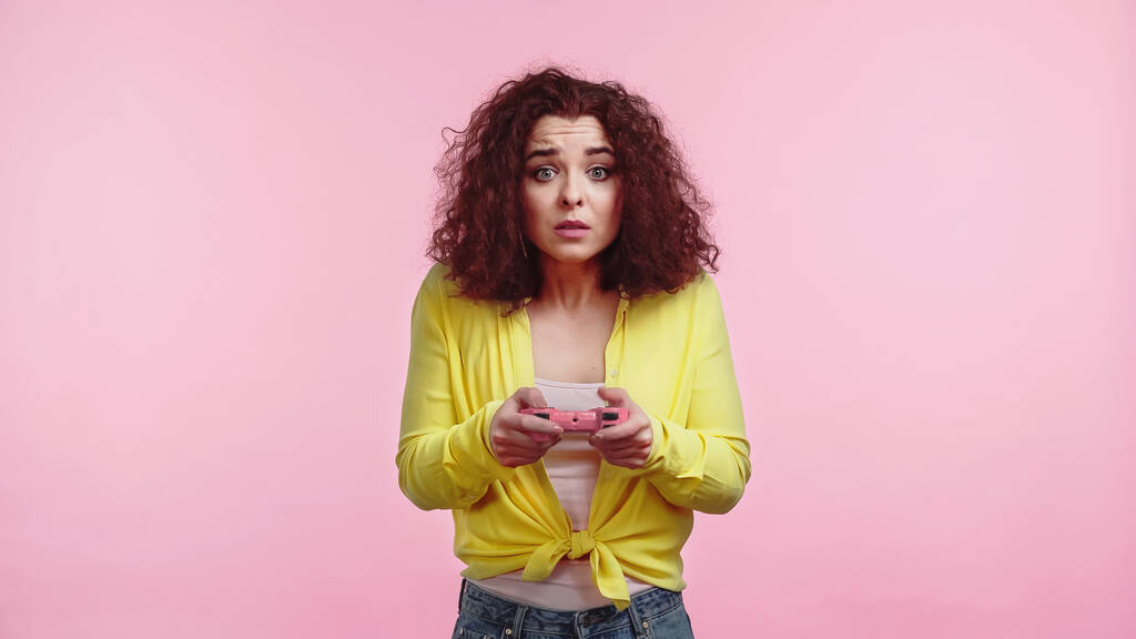 KYIV, UCRAINA - 30 GIUGNO 2021: donna preoccupata che tiene il gamepad e gioca al videogioco isolato su rosa  - Foto, immagini