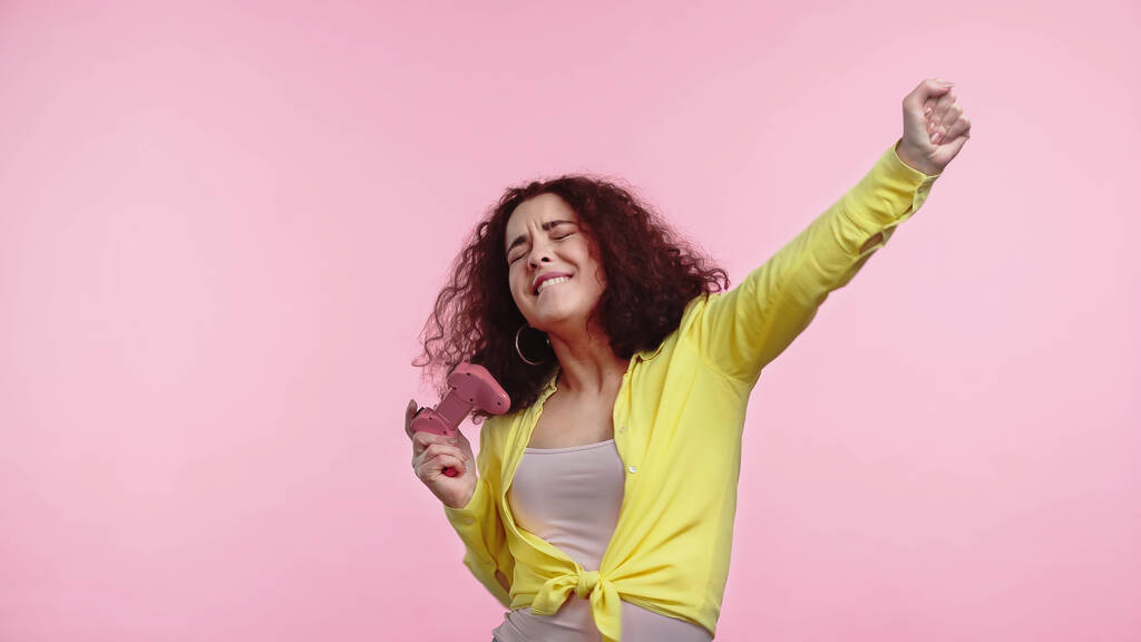 KYIV, UCRAINA - 30 GIUGNO 2021: giovane donna felice che tiene il joystick e gioisce isolata sul rosa  - Foto, immagini