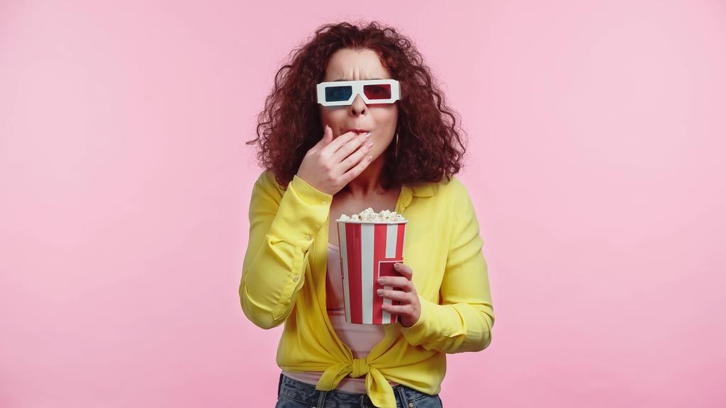 кудрявая женщина в 3D очки держа ведро во время еды попкорн изолирован на розовый  - Фото, изображение
