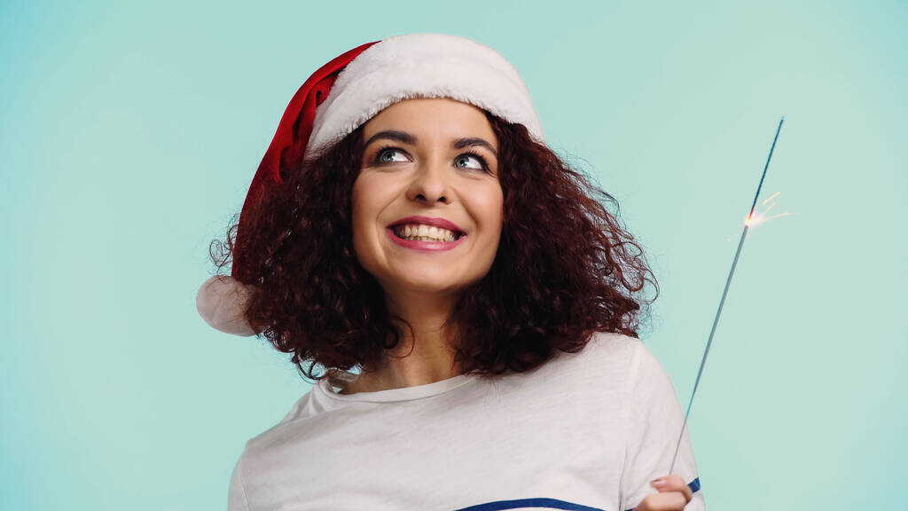 glückliche Frau mit Weihnachtsmütze und Wunderkerze auf blauem Grund - Foto, Bild