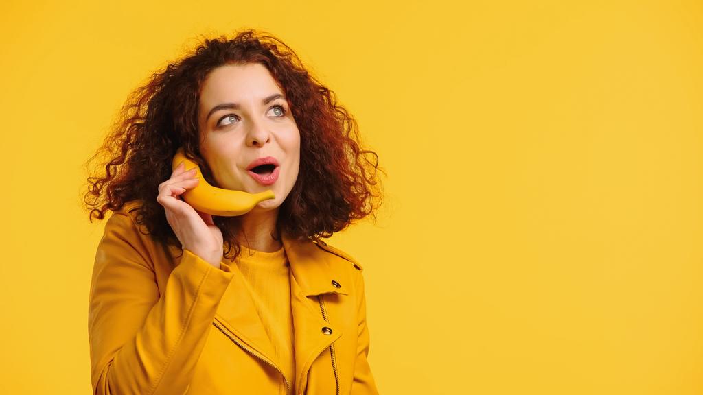 θετική γυναίκα μιμούμενη τηλεφωνική συνομιλία με μπανάνα απομονωμένη στο κίτρινο - Φωτογραφία, εικόνα