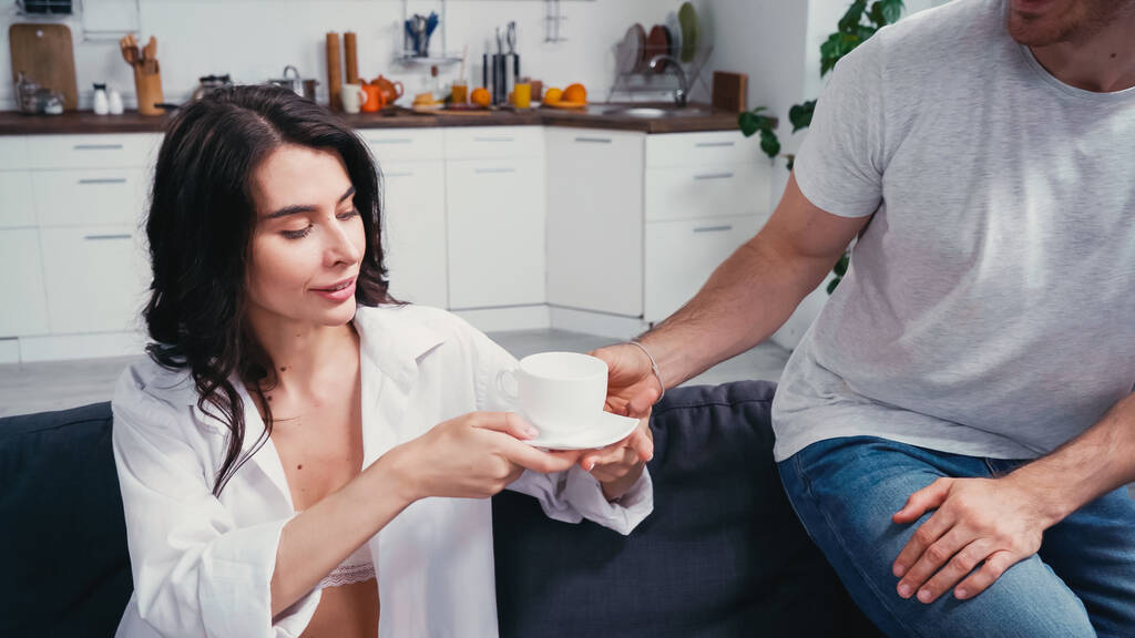 jonge man geven kopje koffie aan vrouw in unbuttoned shirt - Foto, afbeelding