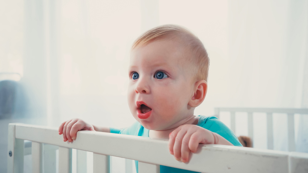 garçon bébé surpris debout dans la crèche de bébé et regardant loin - Photo, image