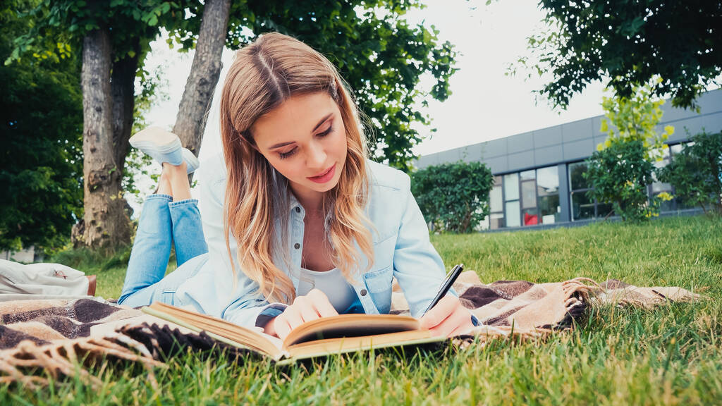 Diák írás, miközben feküdt takarón közel könyv a parkban  - Fotó, kép