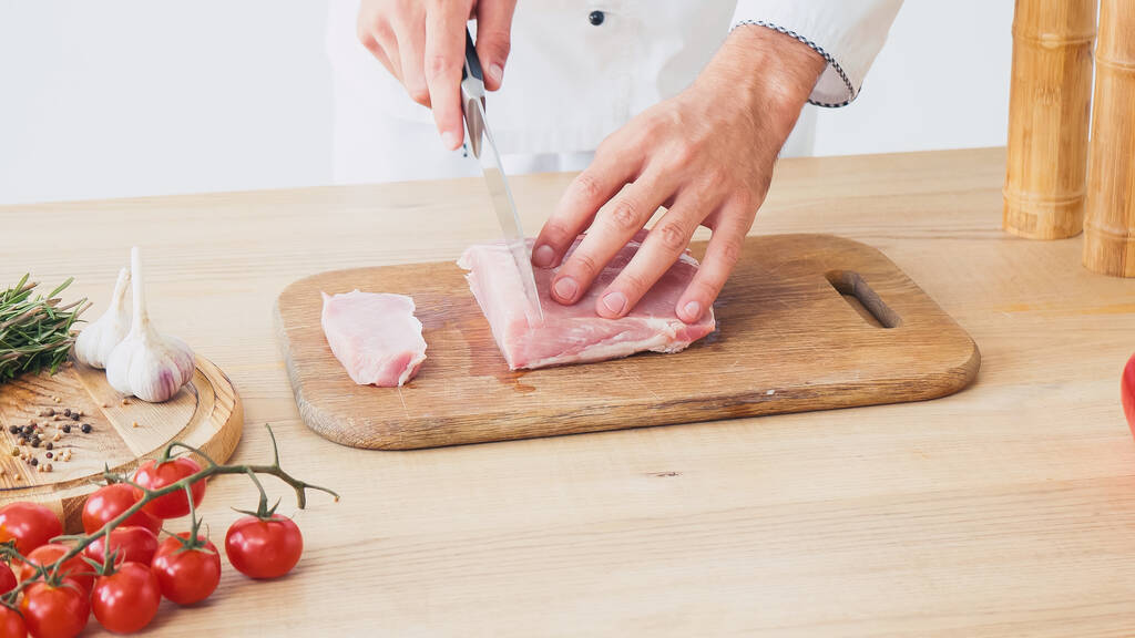 Vista ritagliata del filetto di maiale affettato dallo chef sul tagliere su bianco - Foto, immagini