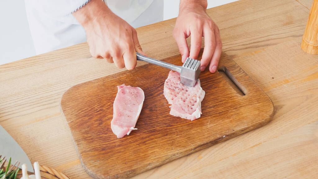 Vista recortada del chef con martillo de corte aplanamiento de cerdo en la mesa - Foto, Imagen