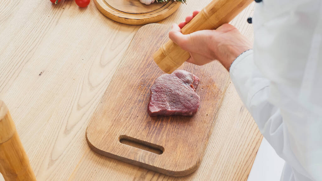 Vista recortada del chef con molino de carne de res condimento filete en la tabla de cortar - Foto, Imagen