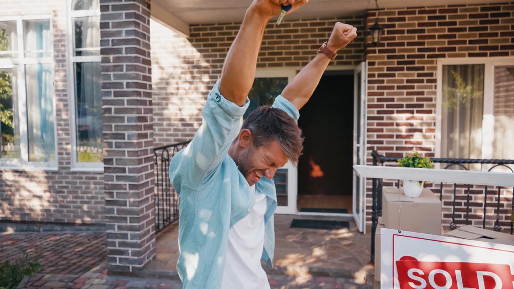 excited man with raised hands near board with sold lettering and new house  - Photo, Image