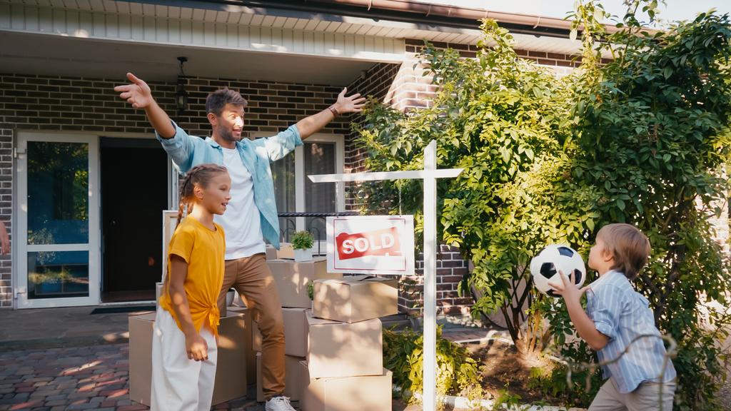 счастливый мальчик проводит футбол рядом с отцом и сестрой в новом доме  - Фото, изображение