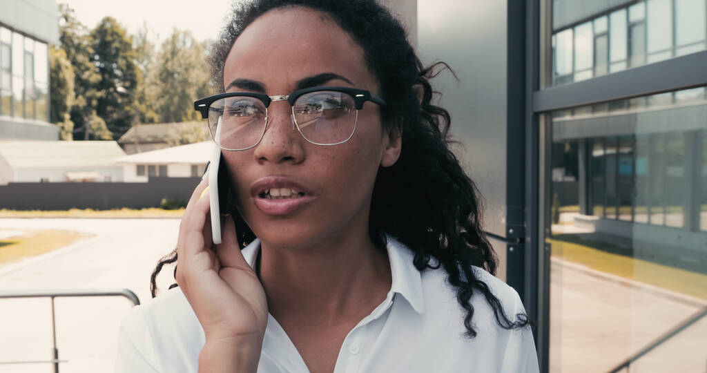 Afroamerikanische Geschäftsfrau telefoniert mit Smartphone in der Nähe von Gebäude - Foto, Bild