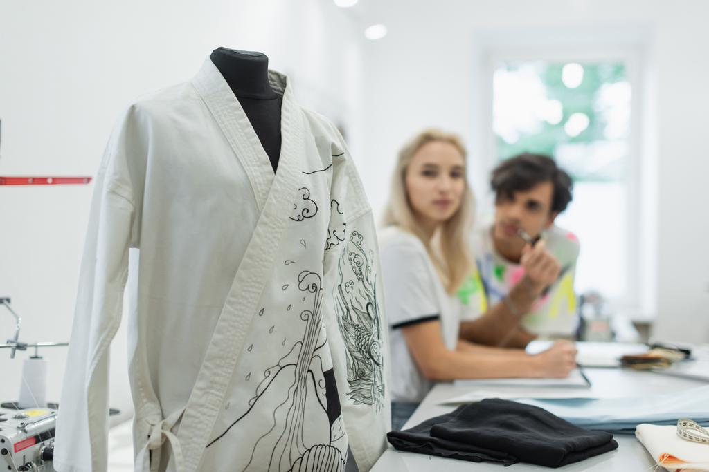 blurred designers looking at kimono with traditional drawing on mannequin in tailor shop - Photo, Image