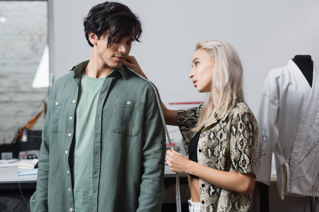 blond naaister meten jonge klant in mode workshop - Foto, afbeelding