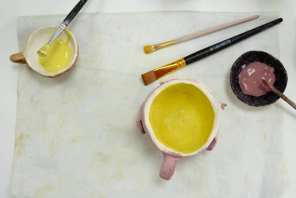 malowanie dziewczynki pędzlem na glinianym kubku ceramicznym w pracowni ceramicznej. Rozwój sztuki i malarstwa u dzieci. Zbliżenie - Zdjęcie, obraz