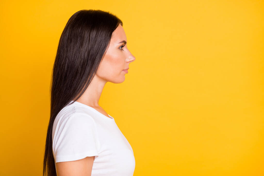 Portrait photo de profil latéral de fille brune en t-shirt regardant l'espace vide avec un visage sérieux isolé sur fond de couleur jaune vif - Photo, image