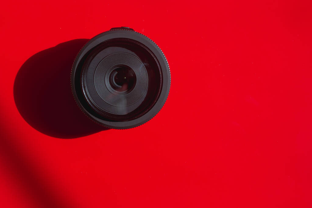 Das Objektiv einer digitalen Spiegelreflexkamera auf rotem Hintergrund. - Foto, Bild
