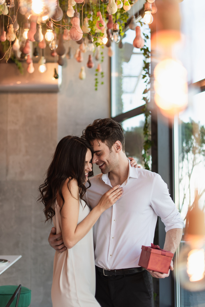 heureux homme tenant boîte cadeau rouge près de petite amie gaie en robe de slip  - Photo, image