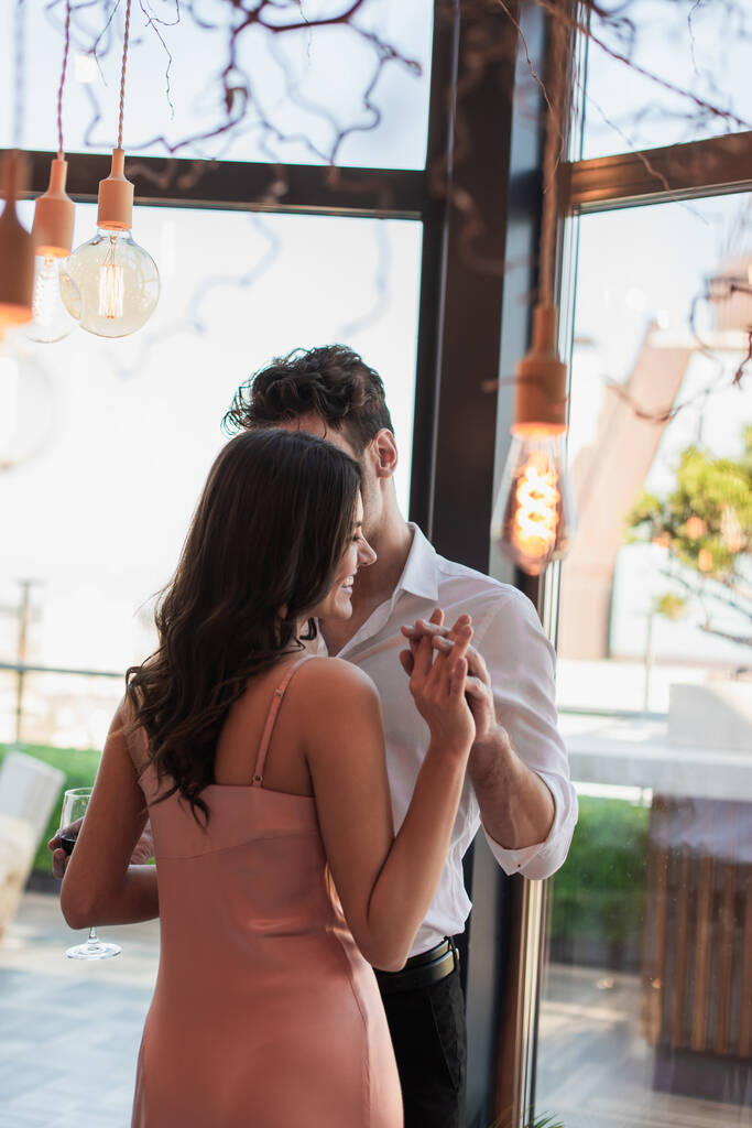 hombre y mujer alegre tomados de la mano en el restaurante cerca de bombillas decorativas  - Foto, imagen