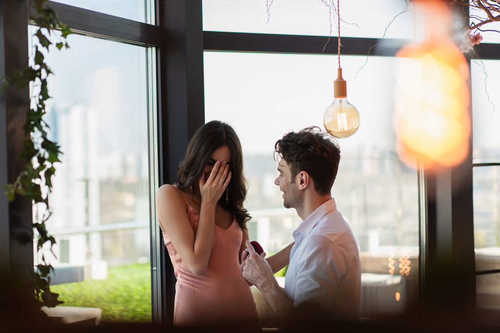 gelukkig man het maken van aanzoek naar vriendin in slip jurk bedekking gezicht in restaurant  - Foto, afbeelding