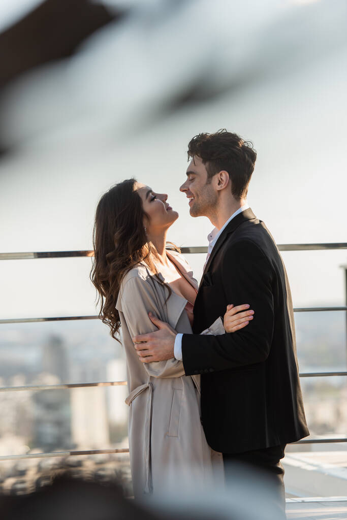 vue latérale d'un homme souriant et d'une femme heureuse se regardant tout en s'embrassant sur la terrasse du restaurant  - Photo, image