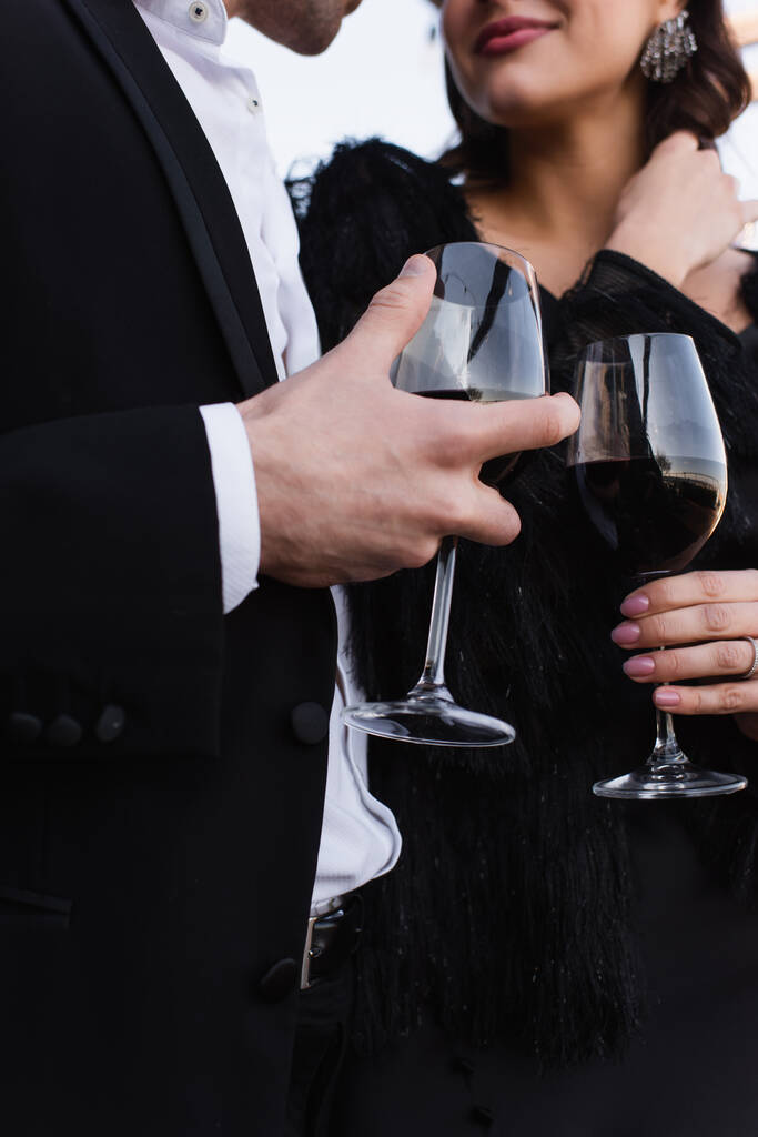 przycięty widok eleganckiej pary trzymających kieliszki czerwonego wina - Zdjęcie, obraz