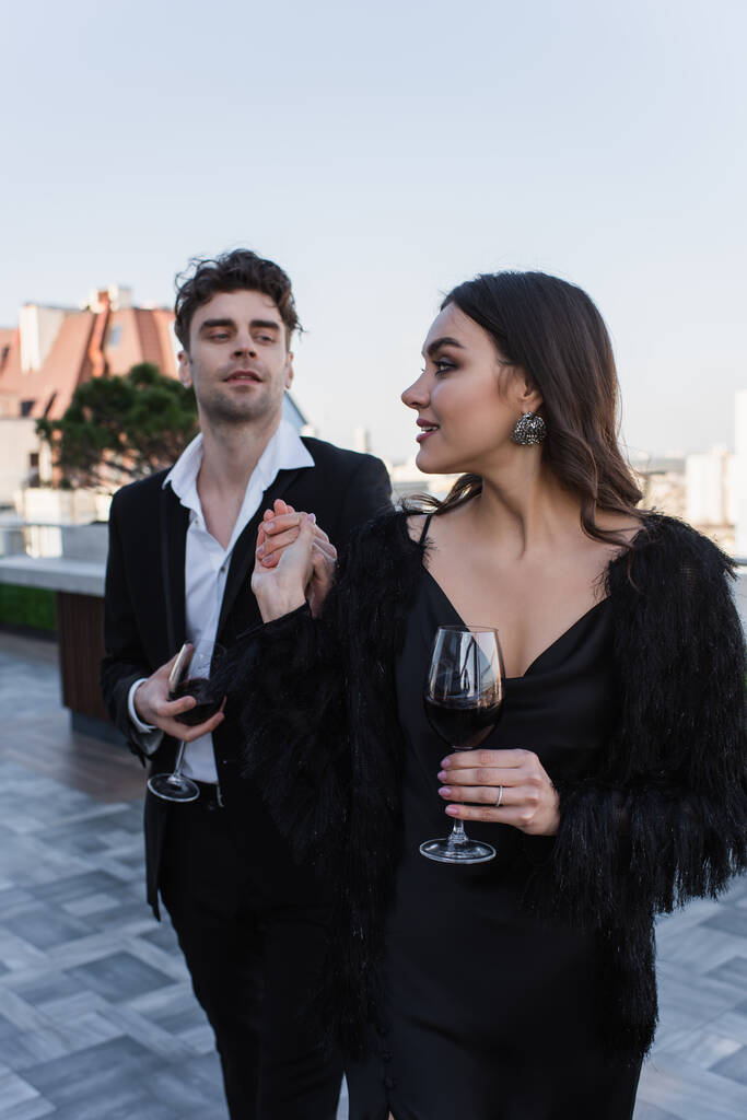 happy woman holding hands with man holding glass of wine on terrace  - Photo, Image