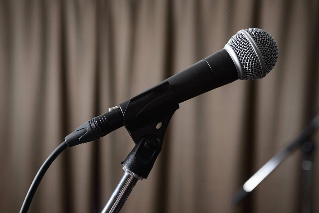 Un micrófono gris en un soporte se para en el escenario sobre el fondo de una cortina marrón. - Foto, Imagen