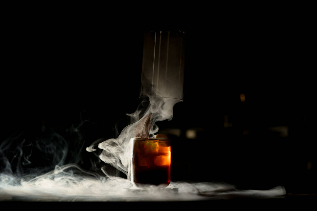 Красивый старомодный стакан холодного напитка в темном баре с прекрасным белым дымом вокруг - Фото, изображение