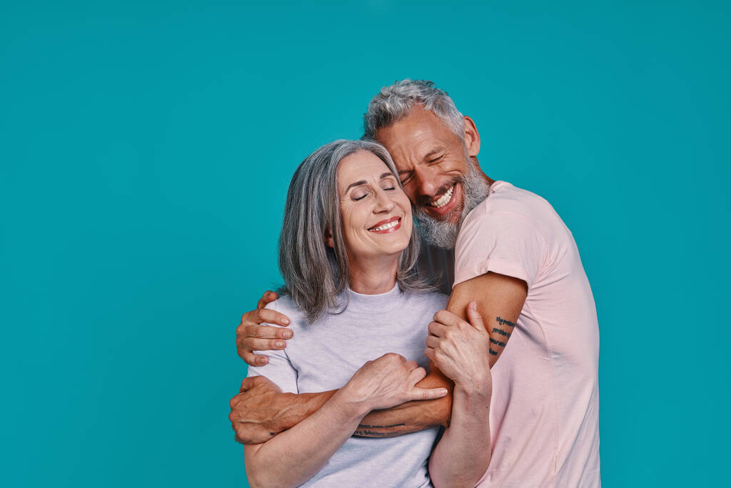 Amare coppia anziana legame e sorridente mentre in piedi insieme contro sfondo blu - Foto, immagini