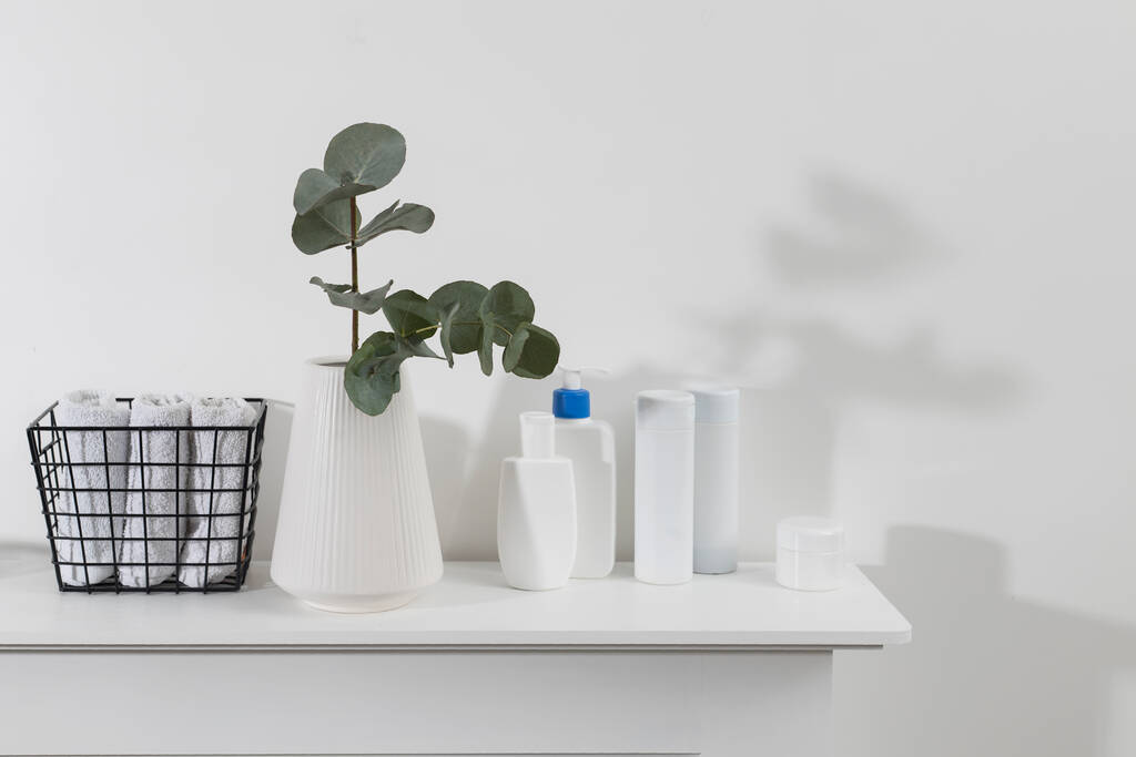Um vaso com um ramo de eucalipto, garrafas de plástico de xampu, creme. Casa de banho. Espaço para SMS. Cesta de metal com toalhas de rosto enroladas - Foto, Imagem
