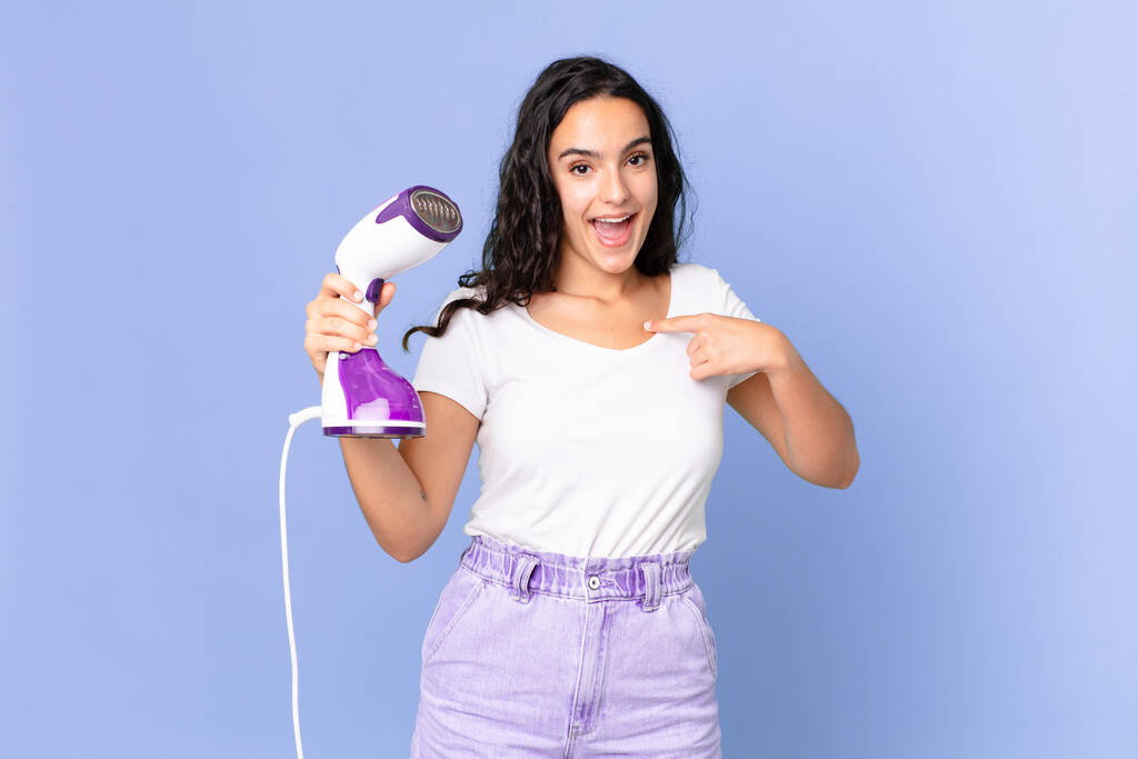 hispanic pretty woman feeling happy and pointing to self with an excited and holding an iron steam - Photo, Image