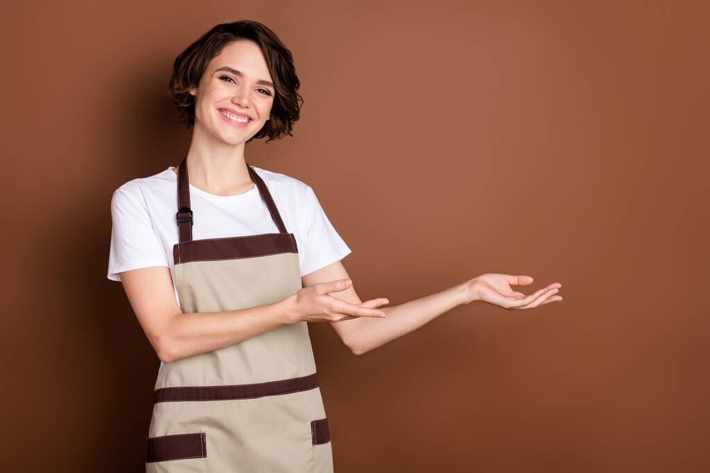 Ritratto di attraente felice allegra ragazza barista caffetteria dimostrando spazio copia benvenuto isolato su sfondo di colore marrone - Foto, immagini