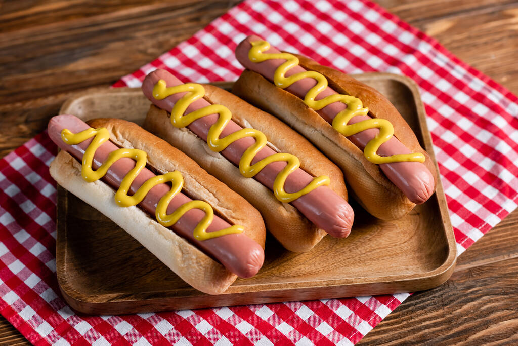 plateau en bois avec de savoureux hot-dogs et serviette à carreaux sur table en bois - Photo, image