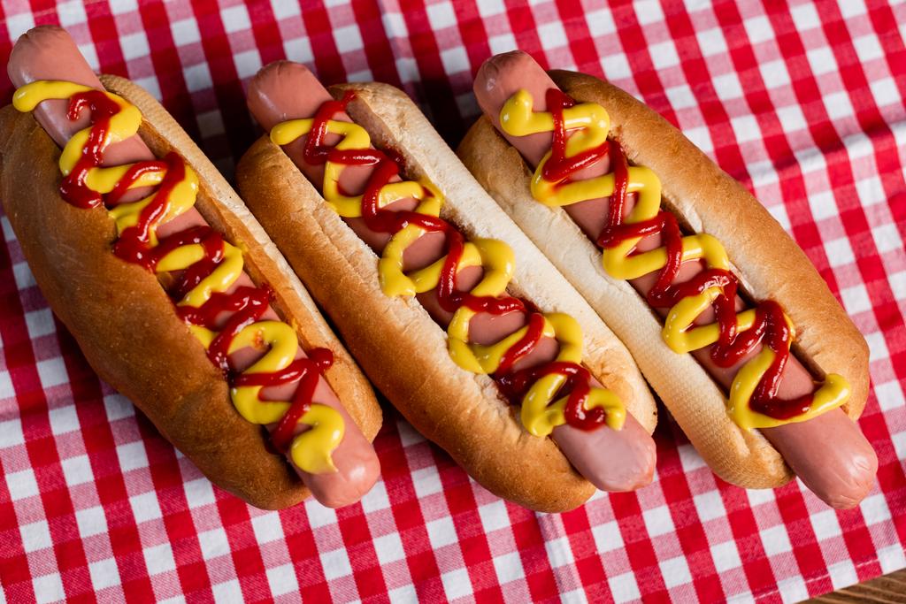 Draufsicht auf köstliche Hot Dogs mit Senf und Ketchup auf karierter Tischdecke - Foto, Bild