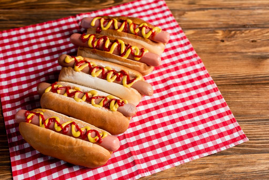 pyszne hot dogi z ketchupem i musztardą oraz serwetka w kratę na drewnianym stole - Zdjęcie, obraz