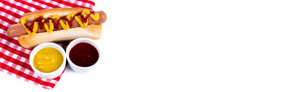 heerlijke hotdog bij ketchup en mosterd op geruite servet geïsoleerd op wit, banner  - Foto, afbeelding