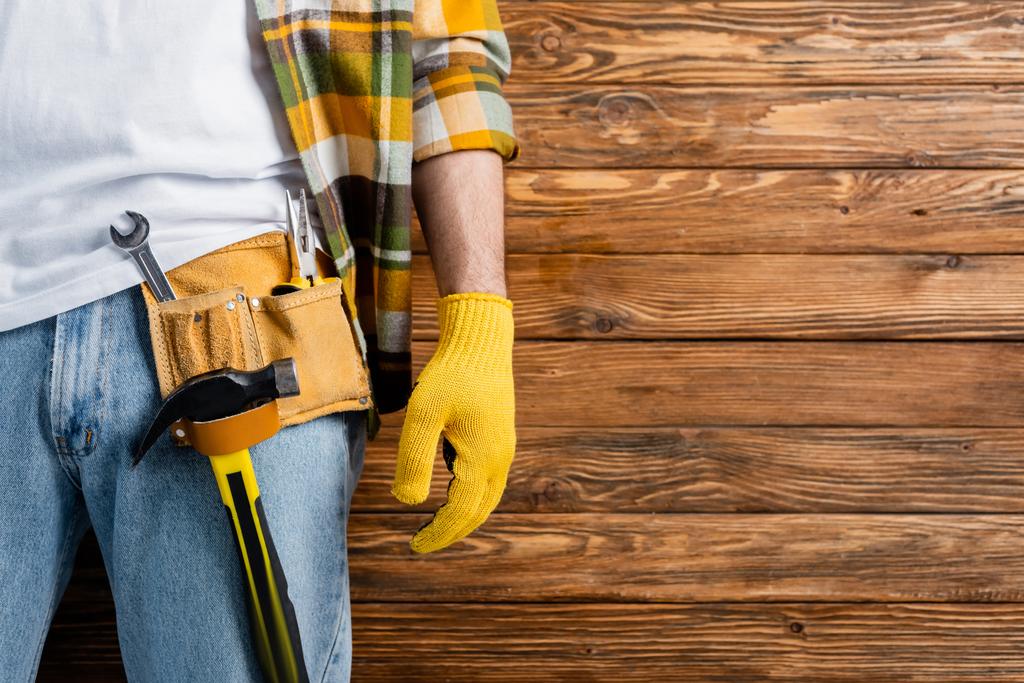 bijgesneden weergave van klusjesman in gereedschapsriem en werkhandschoen op houten achtergrond, arbeidsdag concept - Foto, afbeelding